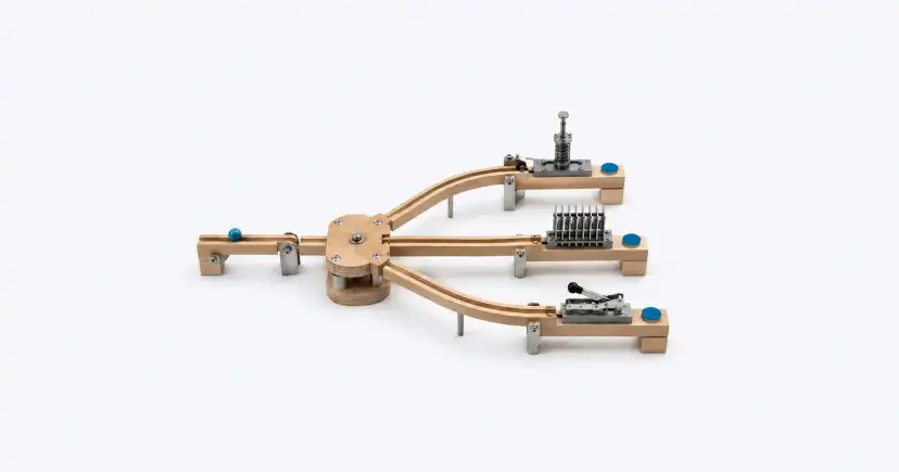 Dispositivo de madera que distribuye tres ramales desde un mecanismo circular hacia módulos diferentes.