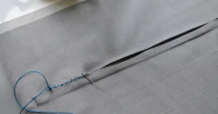 Costura a mano de una tela gris con aguja e hilo azul.