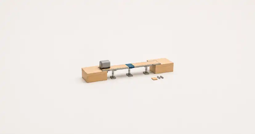 Puente transportador estrecho entre dos bloques de madera, con un cubo y varias piezas sueltas.