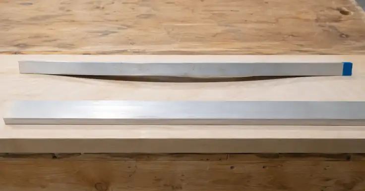Dos barras largas, una blanca y otra oscura, sobre un banco de trabajo de madera.