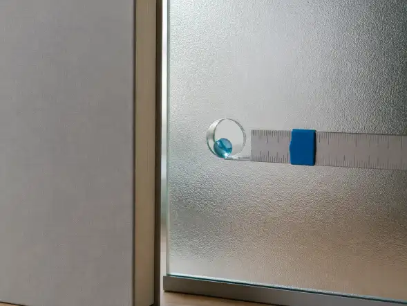 Regla metálica con una lupa de mango azul apoyada sobre un panel de vidrio esmerilado.