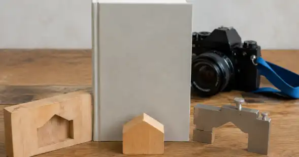Cámara, libro y bloques de madera con huecos y formas geométricas sobre una mesa.