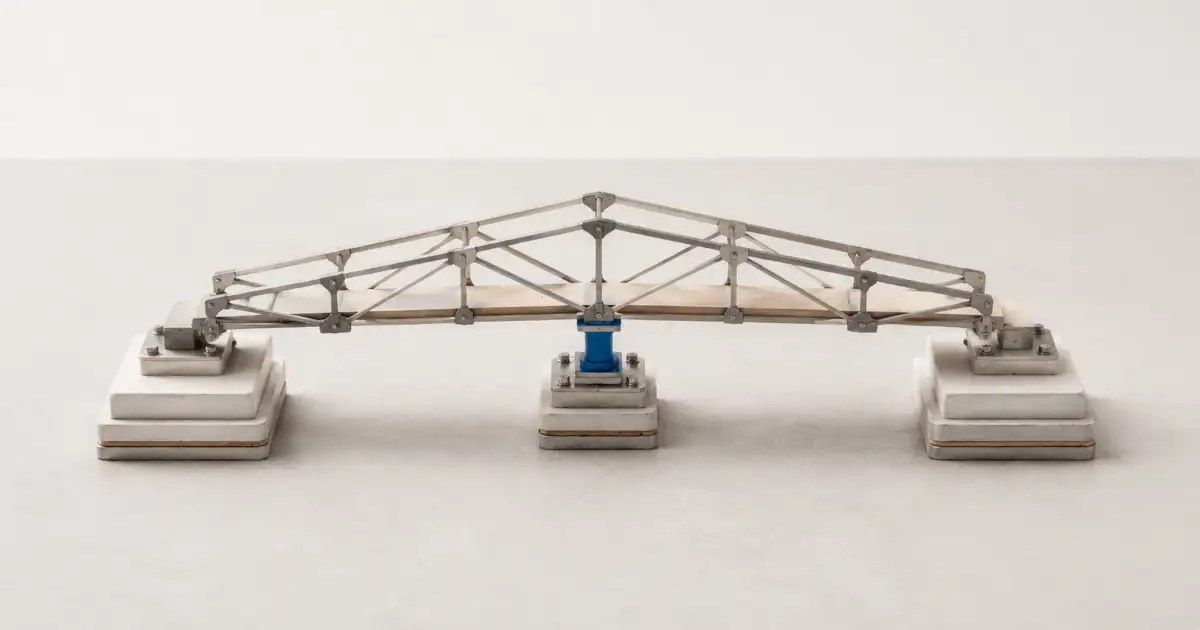 Una estructura de puente metálico se apoya en dos extremos y en un único soporte azul situado bajo el centro.