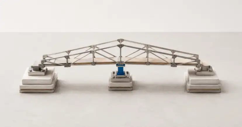 Una estructura de puente metálico se apoya en dos extremos y en un único soporte azul situado bajo el centro.