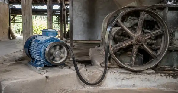 Un motor eléctrico moderno mueve mediante una correa una gran rueda antigua dentro de un taller.