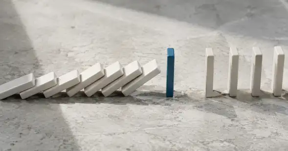 Una cadena de dominós blancos se interrumpe en una ficha azul antes de una segunda fila aún en pie.