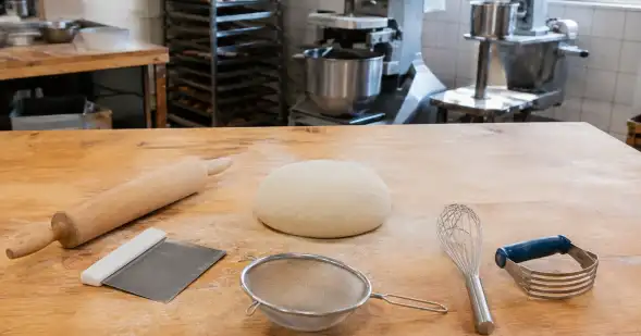 Una mesa de panadería reúne una masa y varias herramientas distintas para trabajarla.