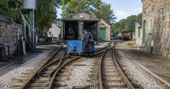 Un trabajador conduce un pequeño vehículo azul por vías ferroviarias que se abren en distintos ramales.