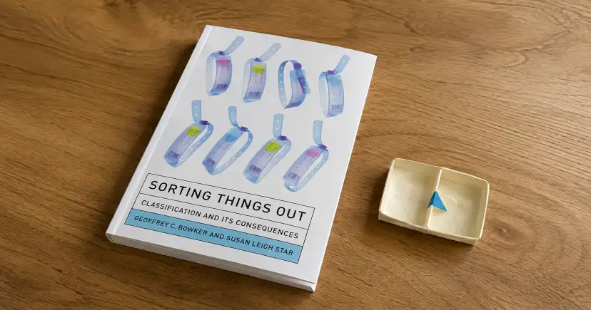 Portada de Sorting Things Out sobre una mesa de madera, junto a una pequeña caja de papel.